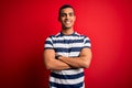 Handsome african american man wearing casual striped t-shirt standing over red background happy face smiling with crossed arms Royalty Free Stock Photo