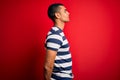 Handsome african american man wearing casual striped t-shirt standing over red background looking to side, relax profile pose with Royalty Free Stock Photo