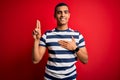 Handsome african american man wearing casual striped t-shirt standing over red background smiling swearing with hand on chest and Royalty Free Stock Photo