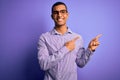 Handsome african american man wearing striped shirt and glasses over purple background smiling and looking at the camera pointing Royalty Free Stock Photo