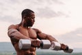 Handsome african american muscular man lifting dumbbells against the sunset sky background Royalty Free Stock Photo