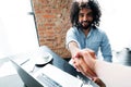 Handsome african american in shirt works at laptop doing handshake with camera while sitting at table Royalty Free Stock Photo