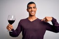 Handsome african american sommelier man tasting glass of red wine over white background with surprise face pointing finger to Royalty Free Stock Photo