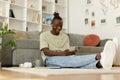 Handsome african american teenager texting while sitting on floor at home on smartphone. Royalty Free Stock Photo