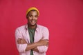 Handsome African American young man posing with hands folded wearing casual pink shirt and yellow hat smiling on camera Royalty Free Stock Photo