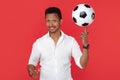 Handsome african american young man spin soccer ball on finger with happy face over red background.