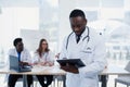 Handsome African doctor in white coat makes some notes. Young medical student with a stethoscope around his neck holds a Royalty Free Stock Photo