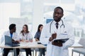 Handsome African doctor in white coat makes some notes. Young medical student with a stethoscope around his neck holds a Royalty Free Stock Photo