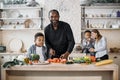 Handsome african father and son preparing tasty salad at kitchen while choping vegetables. Royalty Free Stock Photo
