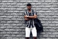 Handsome african man in a cap and shirt with a backpack, against the background of a brick black wall, fashion posing Royalty Free Stock Photo