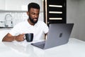 Handsome Afro American businessman is drinking coffee, use laptop in kitchen Royalty Free Stock Photo