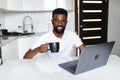 Handsome Afro American businessman is drinking coffee, use laptop in kitchen Royalty Free Stock Photo