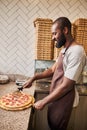 Cheerful young man cutting pepperoni pizza in pizzeria Royalty Free Stock Photo