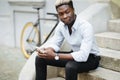 Handsome young Afro American man in casual wear is using smartphone while sitting on stairs outdoors Royalty Free Stock Photo