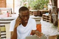 Handsome afro american man with glasses sitting at table in cafe on summer veranda, talking on telephone with closed Royalty Free Stock Photo