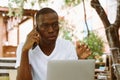 Handsome afro american man with glasses sitting at table in cafe on summer veranda, talking on telephone and working on Royalty Free Stock Photo