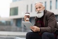 Handsome aged man holding coffee and using digital tablet