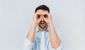 Handsome amazed male wearing blue shirt and white T-shirt holding his hands at his eyes as if looking through binoculars or