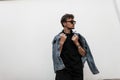 Handsome American young man with stylish hairstyle in denim fashionable clothes in trendy black sunglasses posing near a vintage Royalty Free Stock Photo