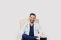 Handsome arab doctor surgeon smiles on white background. Bearded student with stethoscope in medical robe seats in