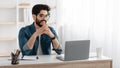 Handsome arab entrepreneur working on laptop computer at home office, sitting at workplace, empty space, panorama