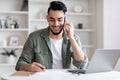 Handsome Arab Male Freelancer Talking On Cellphone And Taking Notes At Home Royalty Free Stock Photo
