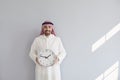 Handsome arab man holding a watch in his hands on a gray background