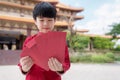 Handsome Asia boy wearing Chinese traditional red suit looking at many red packer monetary gift, red envelop. Standing and smile