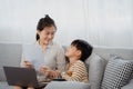 Handsome asian boy and his single mother is working on a laptop computer. The little boy, irritated and nervous, pulled the paper