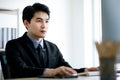 A handsome asian business man wearing formal black suit and necktie, seriously typing and using computer for working with Royalty Free Stock Photo