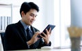 A handsome asian business man wearing formal black suit and necktie, touching a screen of tablet and smiling with happiness while Royalty Free Stock Photo