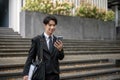 A handsome Asian businessman is checking messages on his phone while walking down the stairs Royalty Free Stock Photo