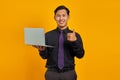 Handsome asian businessman holding laptop smiling and showing thumbs up over yellow background Royalty Free Stock Photo