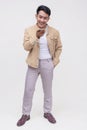 A handsome asian dude in a khaki jacket, white shirt and light gray pants. Holding a cellphone talking to someone via speaker Royalty Free Stock Photo