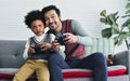 Handsome Asian father smiling with happiness, playing video game at home together with his little adopted African son, exciting