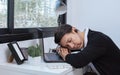 Handsome Asian lazy man wearing casual cloth and earphones, sitting asleep on the table by the window, using laptop for online Royalty Free Stock Photo