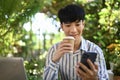 Handsome Asian man drinking coffee and using smartphone outside office building during break Royalty Free Stock Photo