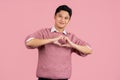 Handsome asian man isolated on light pink background smiling and showing a heart shape with hands Royalty Free Stock Photo