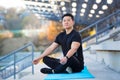 Handsome asian man meditating in modern urban stadium, sitting lotus pose Male practicing yoga mat, zen. relaxes outdoors in Royalty Free Stock Photo