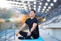 Handsome asian man meditating in modern urban stadium, sitting lotus pose Male practicing yoga mat, zen. relaxes outdoors in Royalty Free Stock Photo