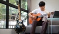 Handsome asian man playing guitar while sitting on couch in living room Royalty Free Stock Photo