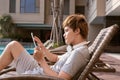 Handsome asian man relaxing by pool and reading e-book Royalty Free Stock Photo