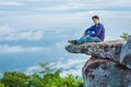 A handsome Asian man is sitting on a large rock that juts out from a steep cliff named Sut Phaen Din. Located at Pa Hin Ngam