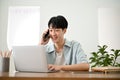 Handsome Asian man talking on the phone and using his laptop computer. work from home Royalty Free Stock Photo