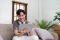 Handsome Asian man using digital tablet while headphones sitting on sofa at home Royalty Free Stock Photo