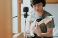 Handsome Asian teenager boy sitting, recording and playing electric guitar with headphone and microphone in bedroom at home Royalty Free Stock Photo