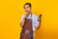 Handsome Asian young man wearing apron holding cell phone and pensive thinking about something with hand on chin Royalty Free Stock Photo