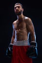 Handsome athletic guy in a red shorts on a black background. The boxer is fetching his breath after practicing hooks and