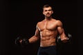 Handsome athletic man in gym is pumping up muscles with dumbbells in a gym. Fitness muscular body on dark Royalty Free Stock Photo