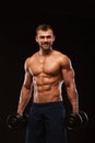 Handsome athletic man in gym is pumping up muscles with dumbbells in a gym. Fitness muscular body isolated on dark Royalty Free Stock Photo